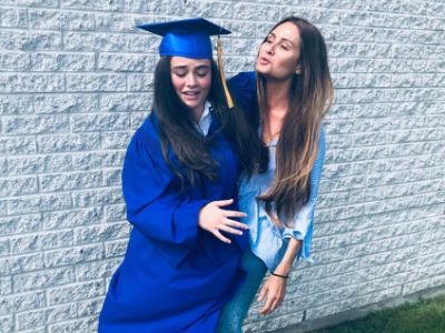 Lola Flanery is in her graduation dress as she and Sacha Grierson are side hugging each other.